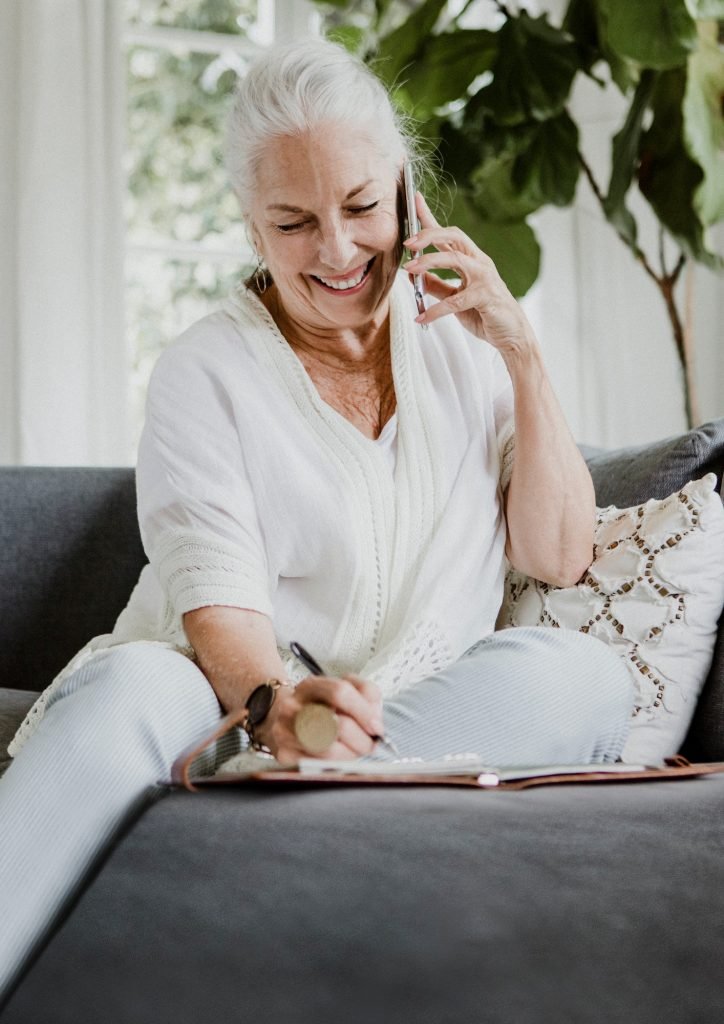 Cheerful elderly woman talking on a phone on a couch